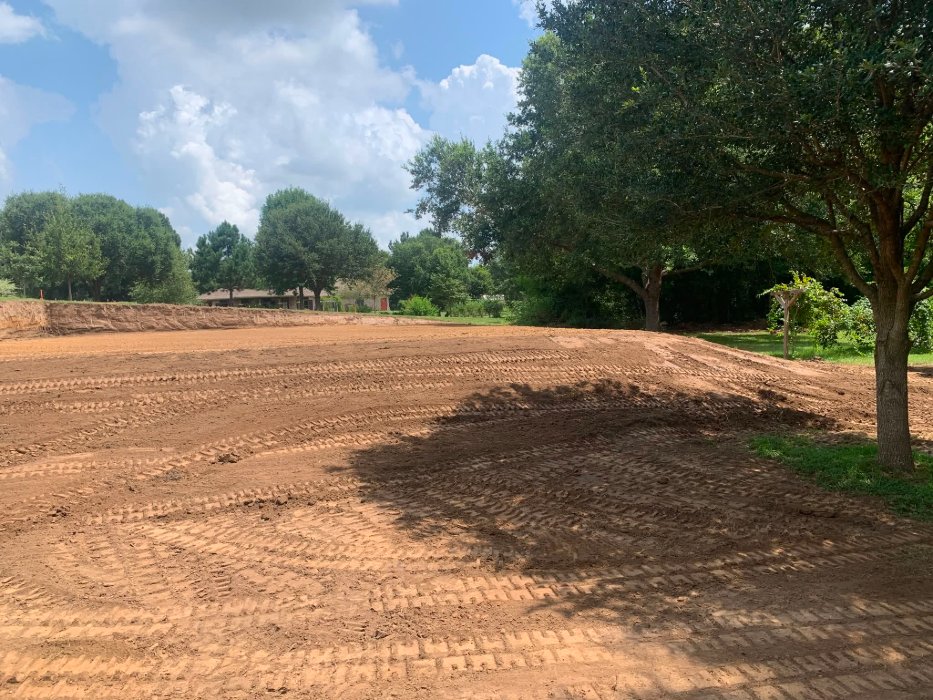 Freshly graded red-dirt house pad under oak trees